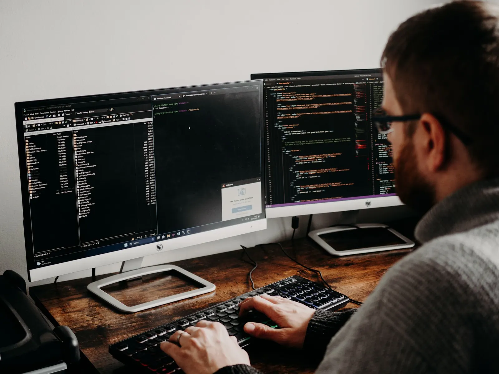 Mitarbeiter mit Brille arbeitet an zwei Bildschirmen mit Programmcode