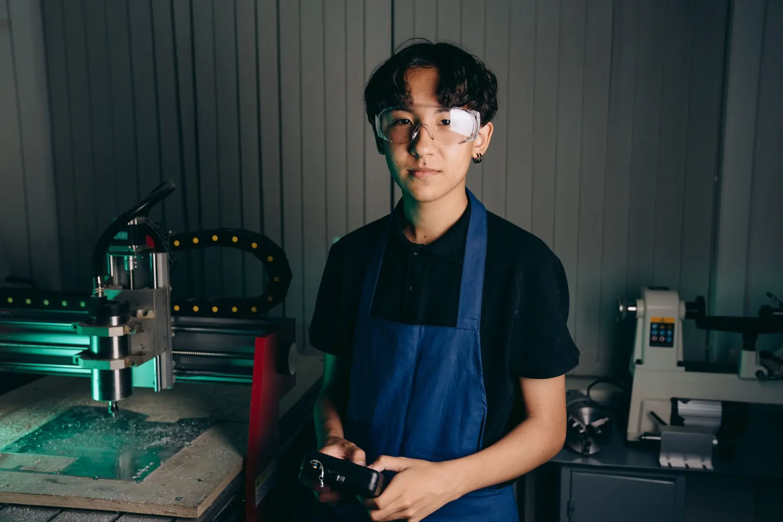 Junger Mitarbeiter mit Schürze und Schutzbrille an einer Maschine in der Werkstatt